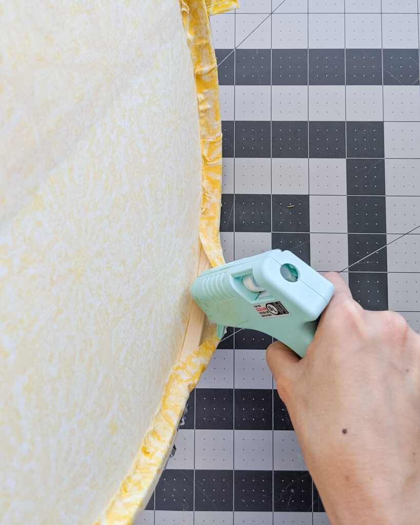 Hot gluing edges of fabric to back of embroidery hoop