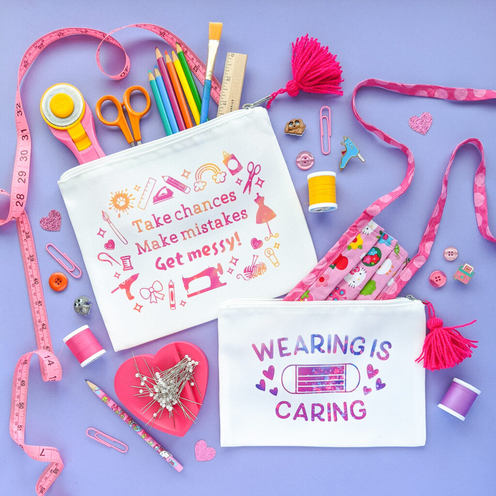 Two white pouches with colorful designs printed on them reading "Take chance, make mistakes, get messy!" and "Wearing is caring" with a face mask. Art and craft supplies are pouring out of the pouches.