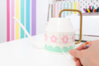 Peeling off clear transfer tape from the pink vinyl flower cutouts on an Ikea Vattenkrasse watering can.