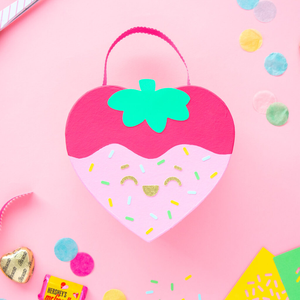 A heart shaped box painted to look like a chocolate-dipped strawberry with sprinkles.